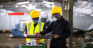 Two employees wearing safety vests discussing workplace safety near a press machine.