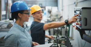 Male and female employees reviewing production data on a control panel to optimize Overall Equipment Effectiveness (OEE) in a manufacturing facility.